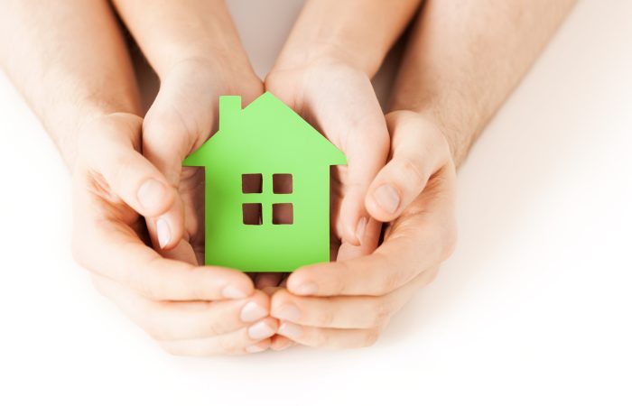 Petite maison verte en papier tenue entre quatre mains