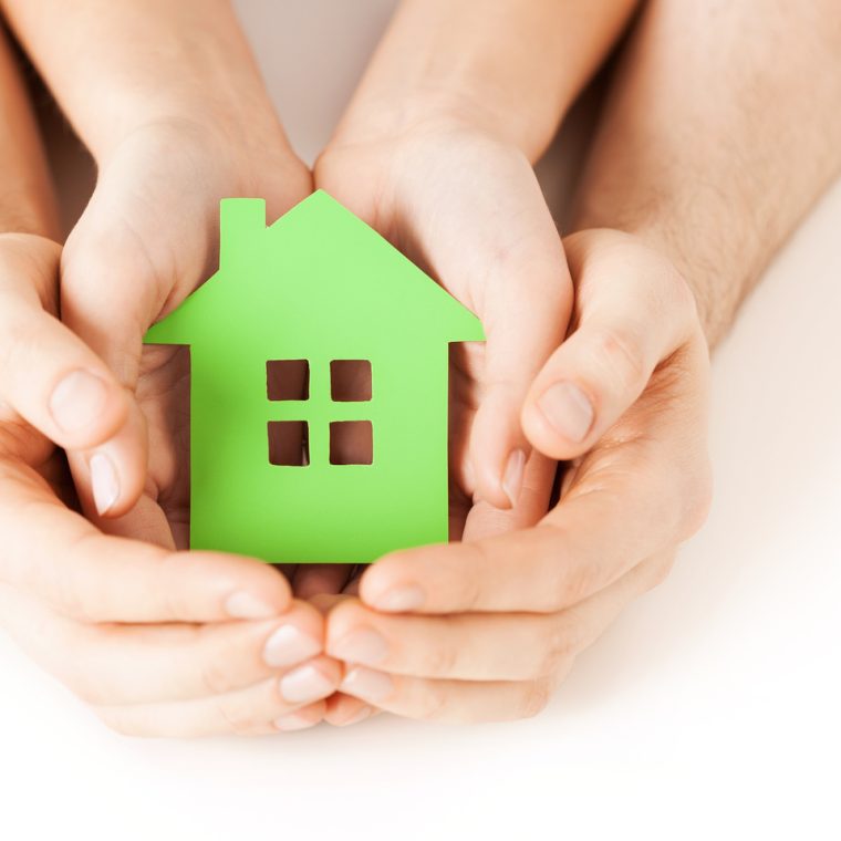 Petite maison verte en papier tenue entre quatre mains